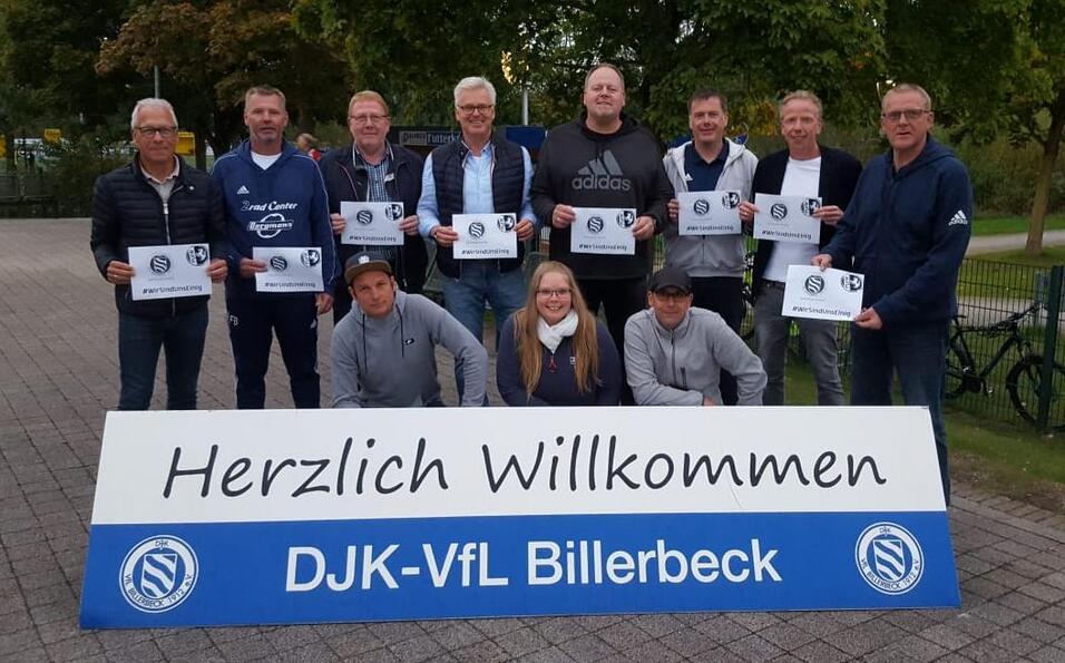 Gruppennaufnahme von zehn Personen, die Plakate halten und vor einem Willkommensschild des DJK-VfL Billerbeck stehen.