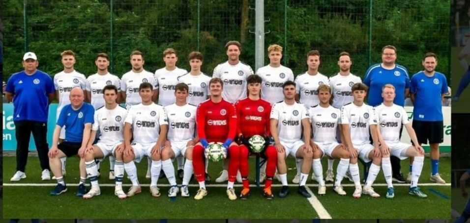 Mannschaftsbild einer Fußballmannschaft in weißen Trikots, mit Trainern und zwei Torhütern in roten Trikots.