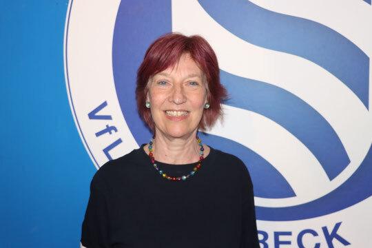L&auml;chelnde Frau mit rotem Haar in einem schwarzen Oberteil vor einem blauen Hintergrund mit dem Logo des VfL L&uuml;beck.