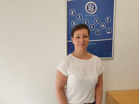 Frau mit kurzen Haaren in wei&szlig;em T-Shirt steht vor einem blauen Plakat mit Symbolen sportlicher Aktivit&auml;ten.