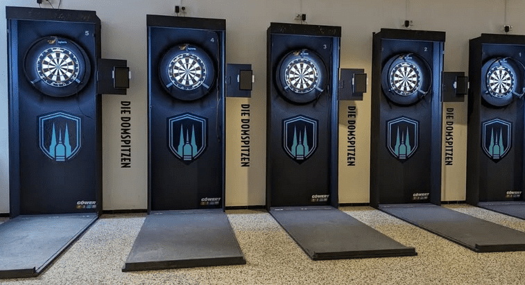 Sechs Dartscheiben an Wänden mit schwarzem Design, beschriftet mit „DIE DOMSPITZEN“, auf einem glatten Boden.