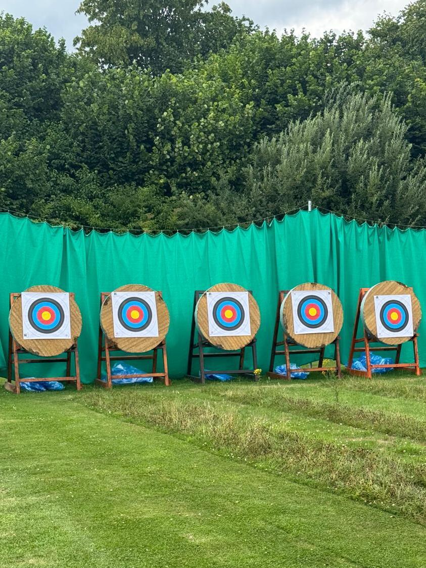 Sechs Zielscheiben mit bunten Mittelpunkt stehen auf einem Rasenfeld, hinter einem grünen Sichtschutz.