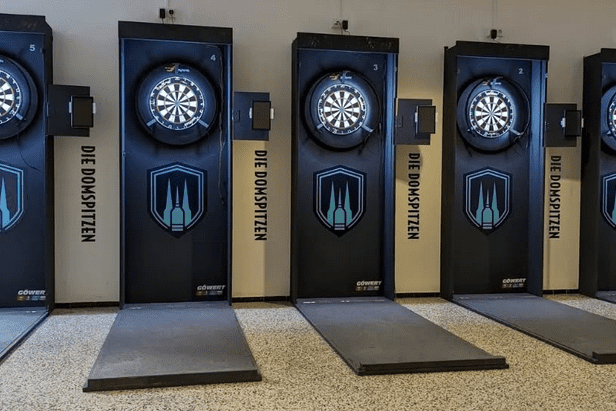 Sechs Dartscheiben an W&auml;nden mit schwarzem Design, beschriftet mit &bdquo;DIE DOMSPITZEN&ldquo;, auf einem glatten Boden.